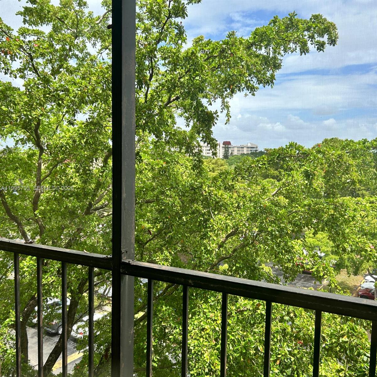 A view of trees and a distant building from a screened-in balcony with railings — 3771 Environ Blvd # 650, Lauderhill FL 33319, LAUDERHILL, FL