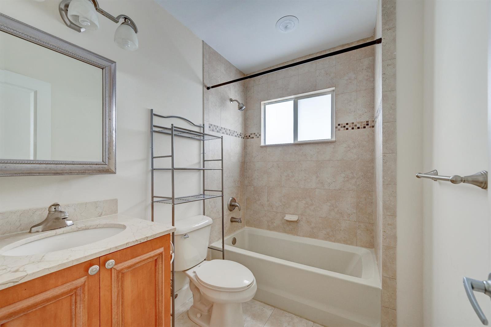 A bathroom features a vanity, toilet, and a bathtub with a shower head and window — 410 SW 15th Street # 204, Pompano Beach FL 33060, POMPANO BEACH, FL