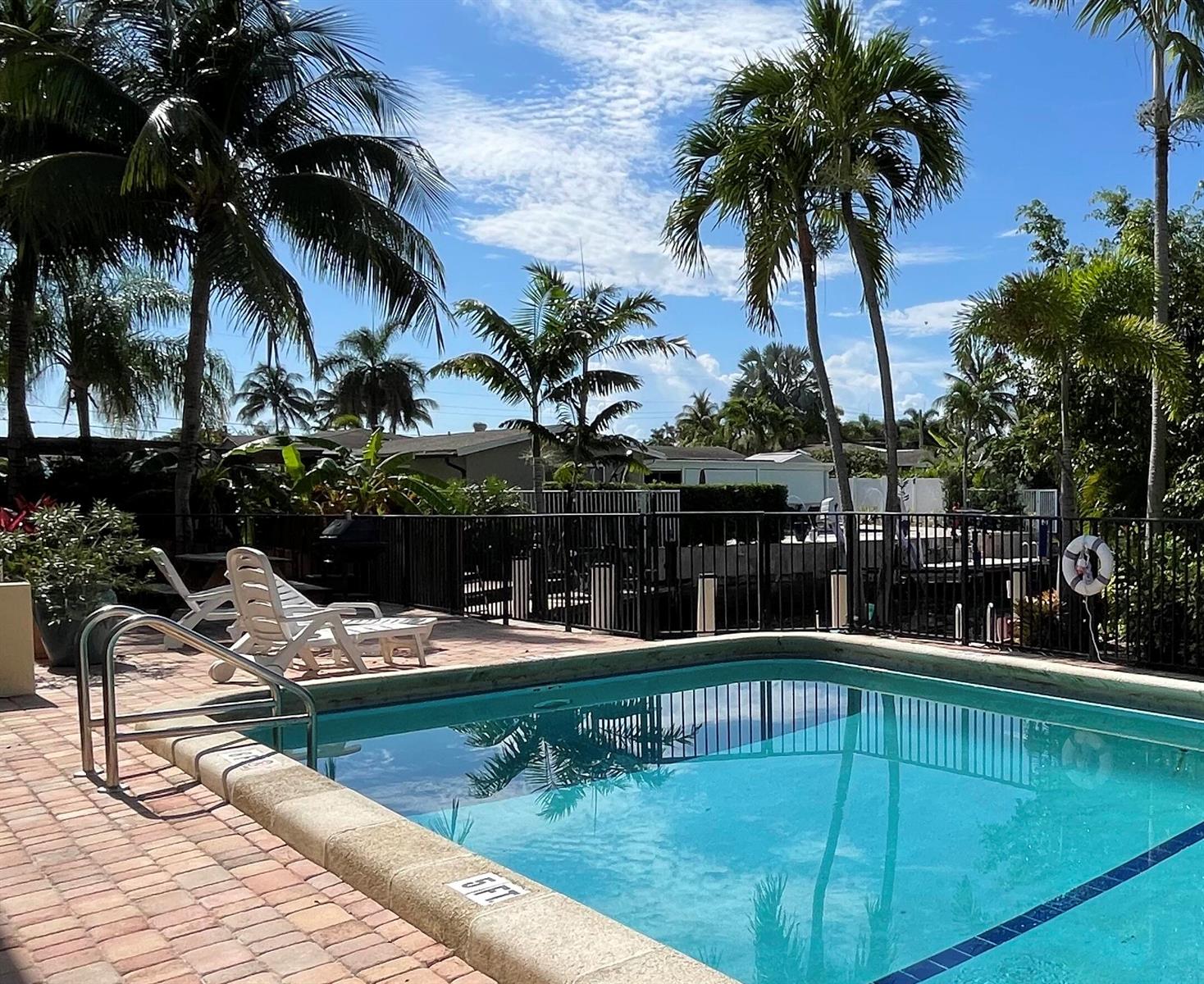 A swimming pool with a brick deck, lounge chairs, and palm trees under a blue sky — 410 SW 15th Street # 204, Pompano Beach FL 33060, POMPANO BEACH, FL