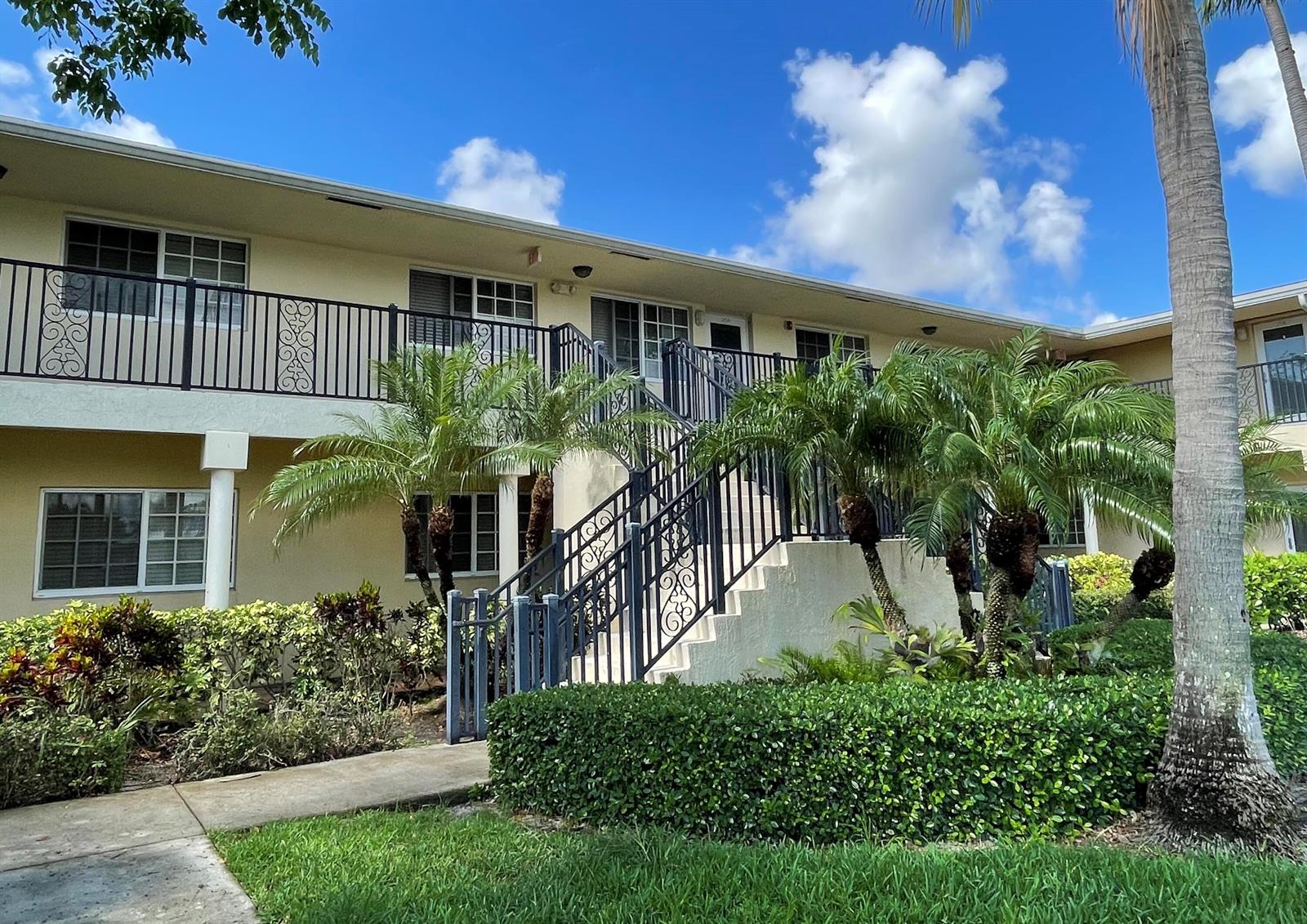 A two-story apartment building exterior features a central staircase with black metal railings and landscaping — 410 SW 15th Street # 204, Pompano Beach FL 33060, POMPANO BEACH, FL