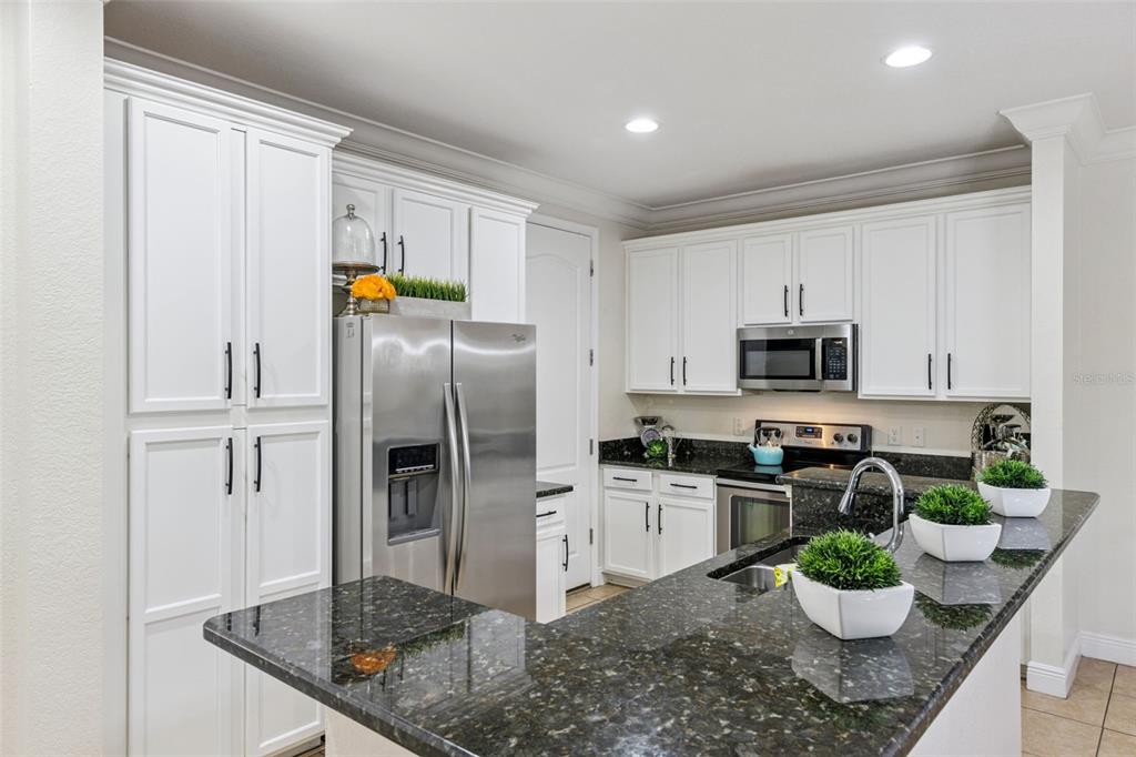 A kitchen features white cabinetry, stainless steel appliances, and dark granite countertops — 8410 KELSALL DRIVE, ORLANDO, FL