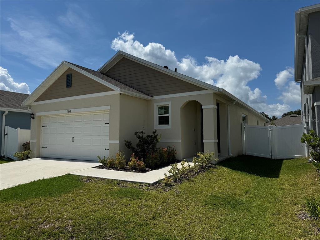 A single-story house with a beige stucco exterior, a two-car garage, and a white fence — 1648 HEART BAR ROAD, KISSIMMEE, FL