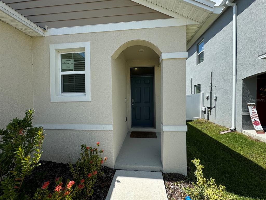The exterior of a house features a beige stucco facade, a dark door, and landscaping — 1648 HEART BAR ROAD, KISSIMMEE, FL