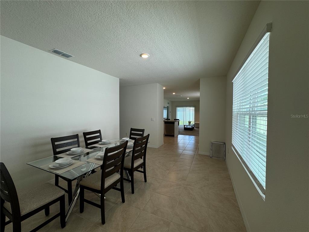 A dining area with a glass table and chairs leads to an open kitchen and living space — 1648 HEART BAR ROAD, KISSIMMEE, FL
