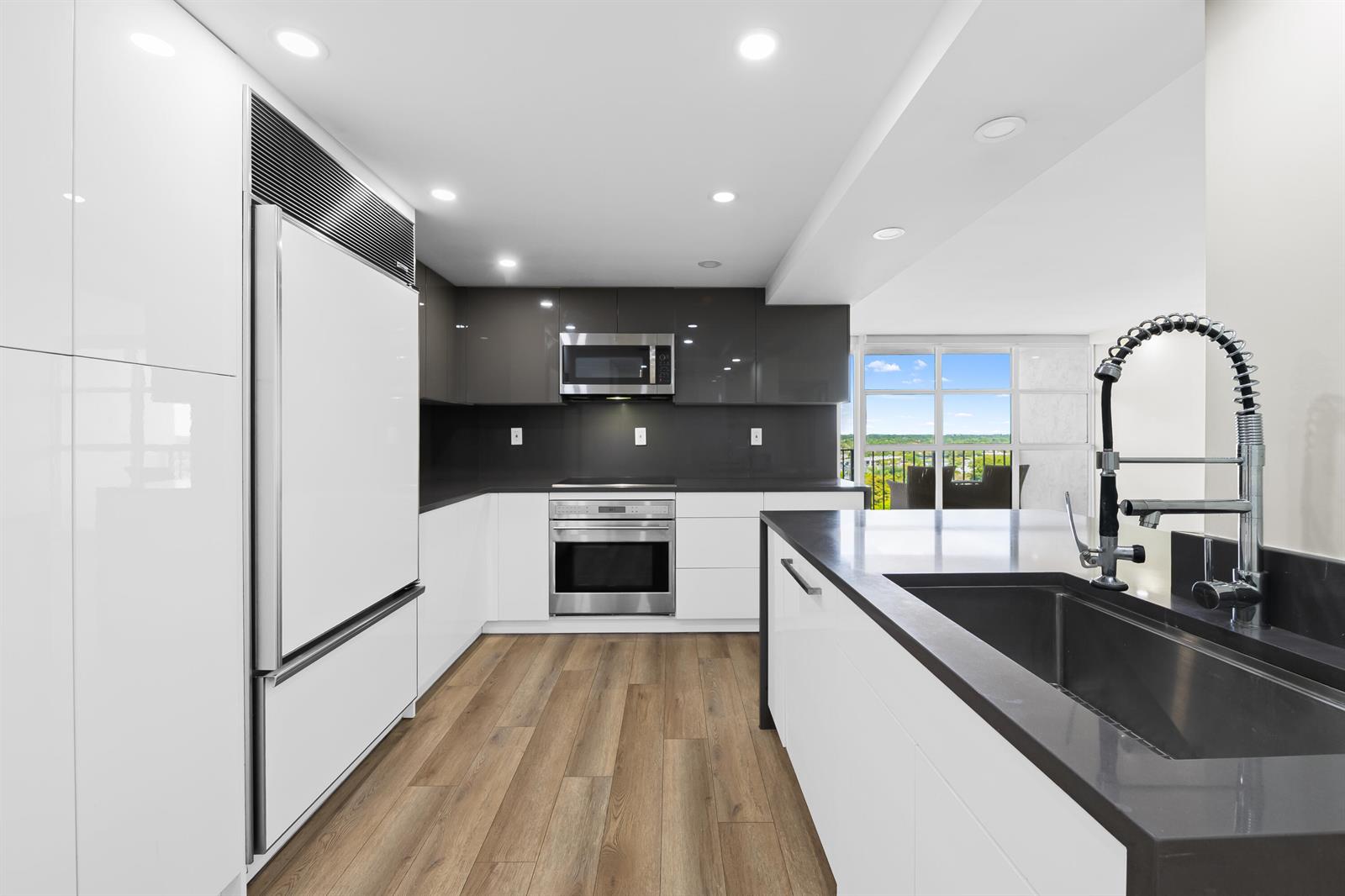 A modern kitchen features white and dark grey cabinetry, stainless steel appliances, and wood flooring — 600 Parkview Drive # 1029, Hallandale Beach FL 33009, HALLANDALE BEACH, FL
