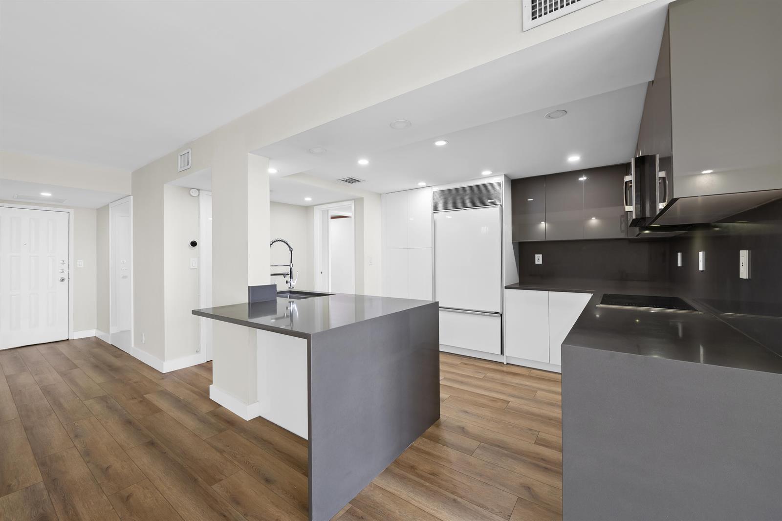 A modern kitchen features dark gray countertops, white cabinetry, and wood-look flooring — 600 Parkview Drive # 1029, Hallandale Beach FL 33009, HALLANDALE BEACH, FL