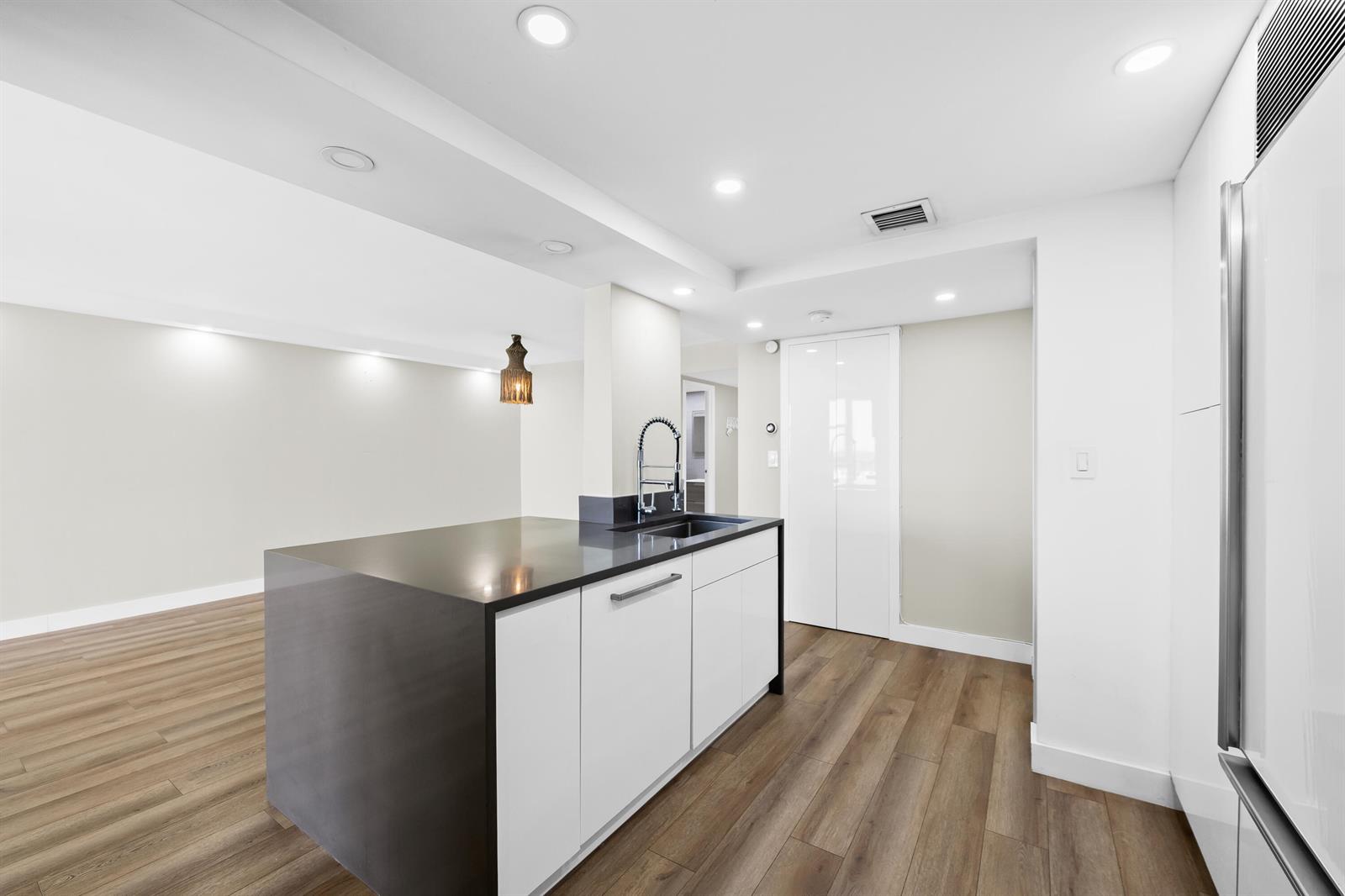 A modern kitchen featuring a dark countertop island, white cabinetry, and light wood-look flooring — 600 Parkview Drive # 1029, Hallandale Beach FL 33009, HALLANDALE BEACH, FL