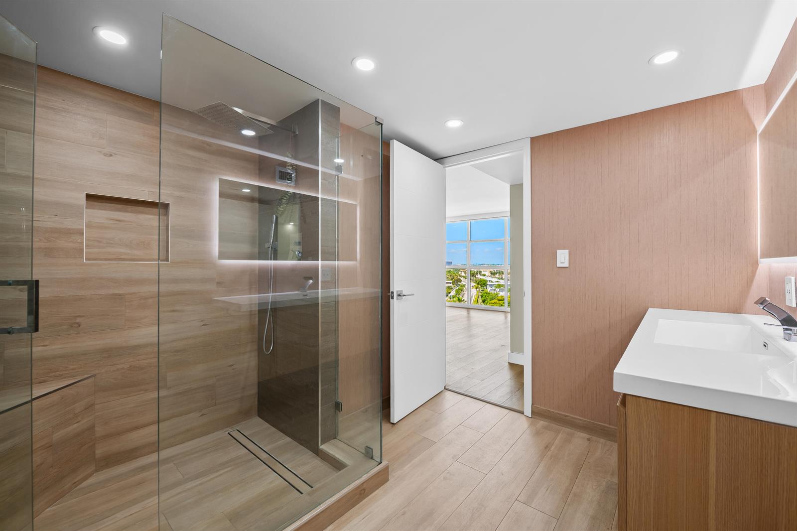 A modern bathroom features a glass-enclosed shower, wood-look tile, and a white vanity — 600 Parkview Drive # 1029, Hallandale Beach FL 33009, HALLANDALE BEACH, FL