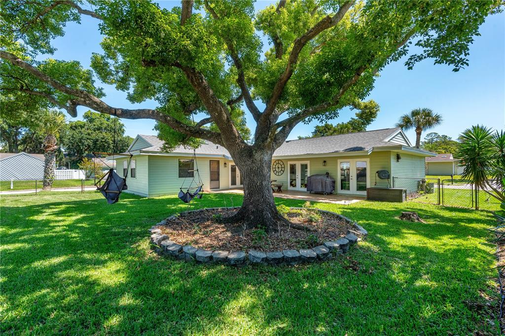 A large tree with a stone border stands in the backyard of a light-green house — 2916 FOXCROFT LANE, SOUTH DAYTONA, FL