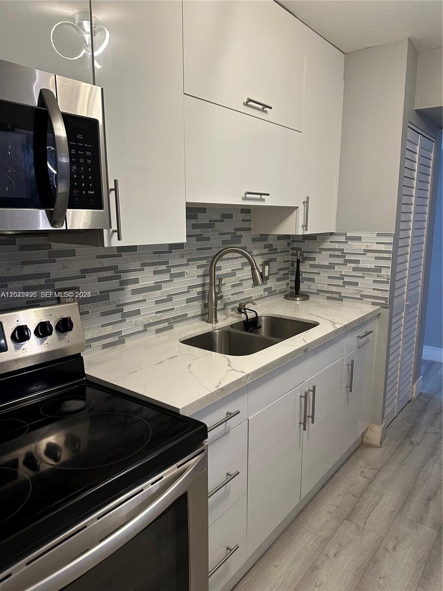 A modern kitchen features white cabinets, stainless steel appliances, and a gray tiled backsplash — MIAMI, FL