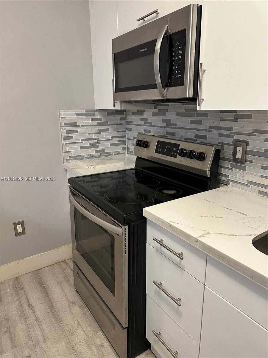 A kitchen features stainless steel appliances, white cabinets, and a gray-toned tiled backsplash — MIAMI, FL