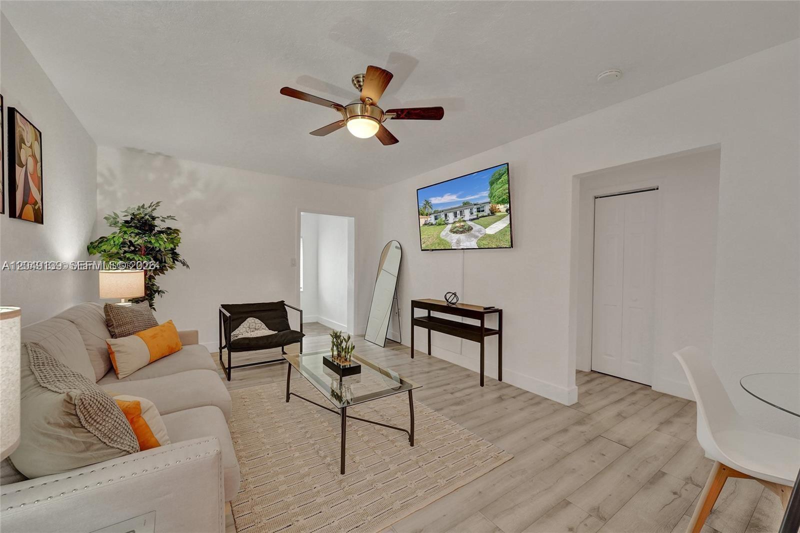 A living room features a beige sofa, glass coffee table, wall-mounted television, and wood-look flooring — 361 NW 103rd St, Miami FL 33150, MIAMI, FL