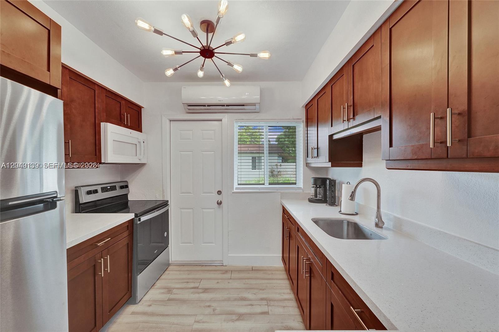 A galley kitchen features wood cabinets, white countertops, stainless steel appliances, and a modern chandelier — 361 NW 103rd St, Miami FL 33150, MIAMI, FL