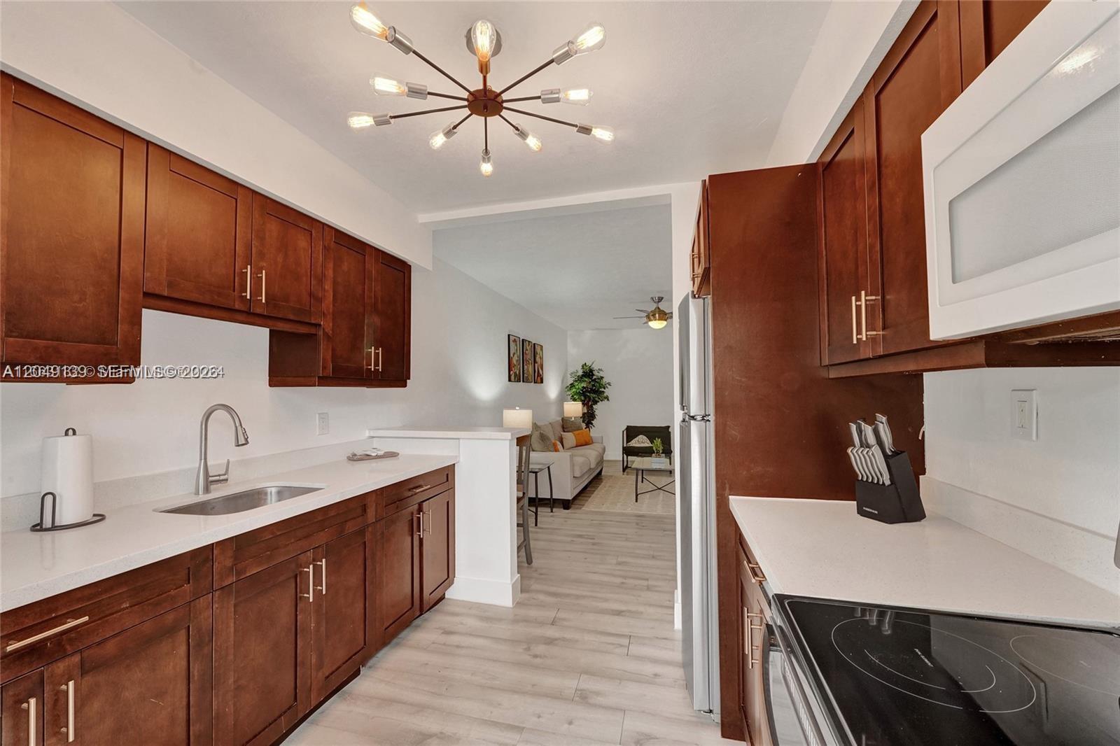 A galley kitchen features dark wood cabinets, white countertops, and a modern sputnik light fixture — 361 NW 103rd St, Miami FL 33150, MIAMI, FL