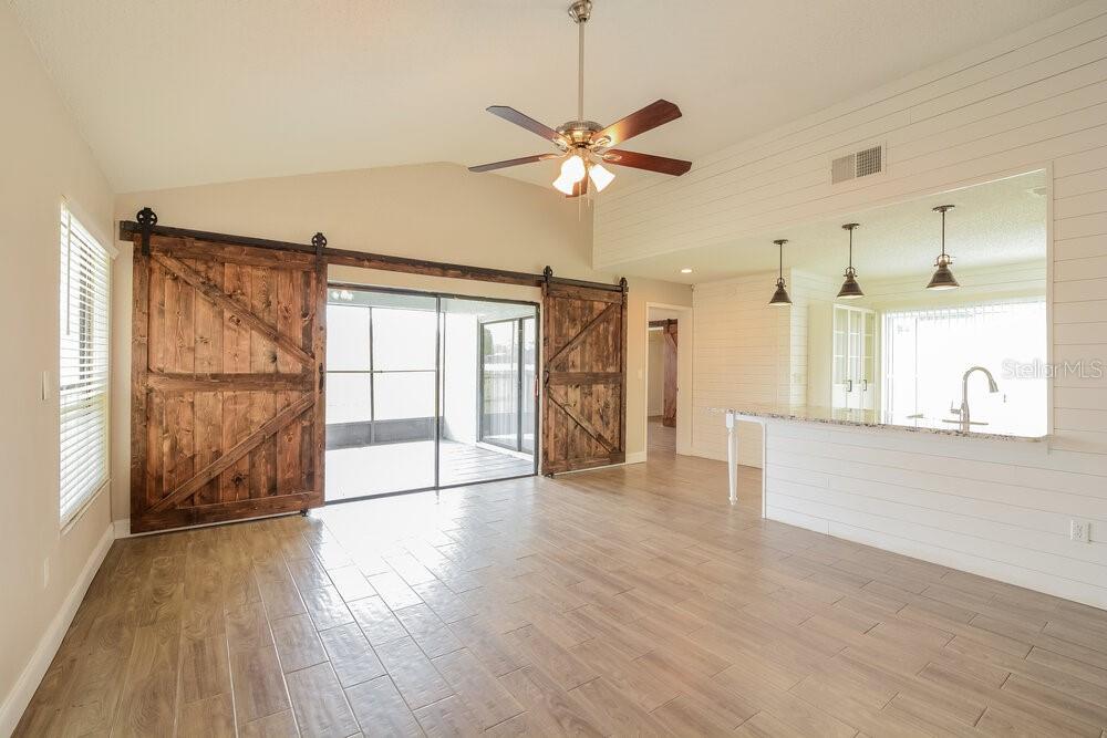 A living room features wood-look tile floors, sliding barn doors, and a kitchen pass-through window — 3510 BUFFAM PLACE, CASSELBERRY, FL