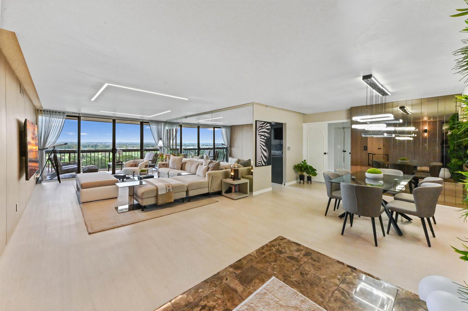 A spacious living and dining area features light wood floors, floor-to-ceiling windows, and mirrored walls — 1900 Consulate Place # 1205, West Palm Beach FL 33401, WEST PALM BEACH, FL