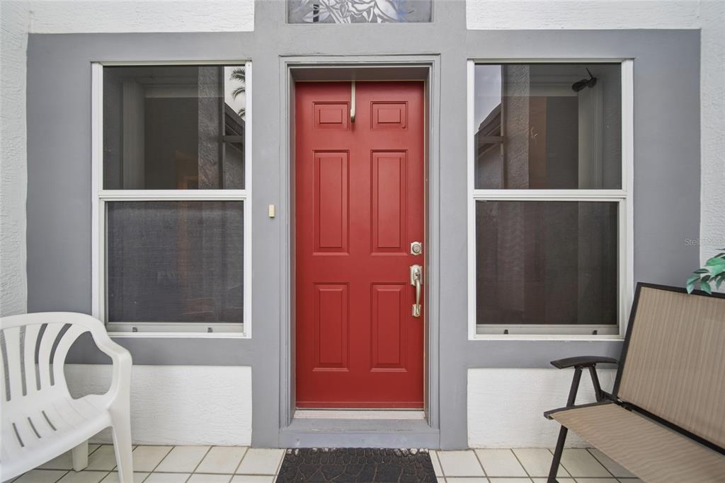 A red front door is centered between two windows on a tiled porch — 8051 THATCH TERRACE, HUDSON, FL