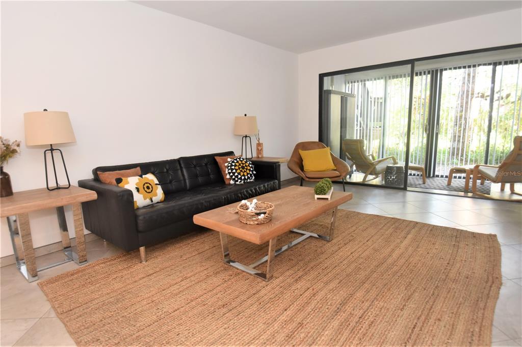 A living room features a black leather sofa, a wooden coffee table, and a sliding door — 1716 GLENHOUSE DRIVE UNIT GL323, SARASOTA, FL