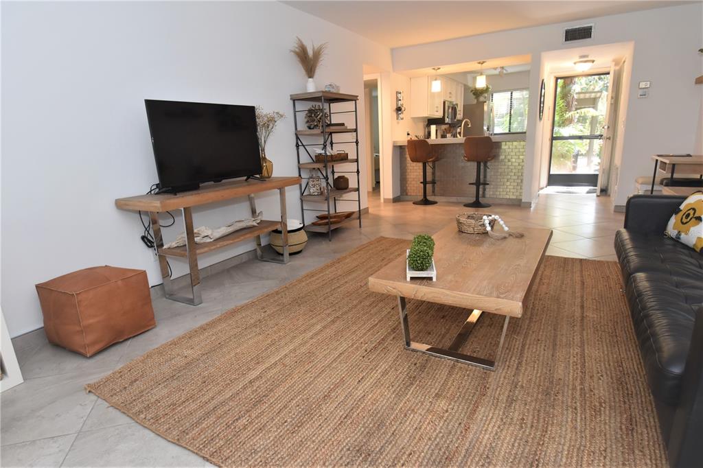 A living room features a television console, a coffee table, and an open kitchen area — 1716 GLENHOUSE DRIVE UNIT GL323, SARASOTA, FL