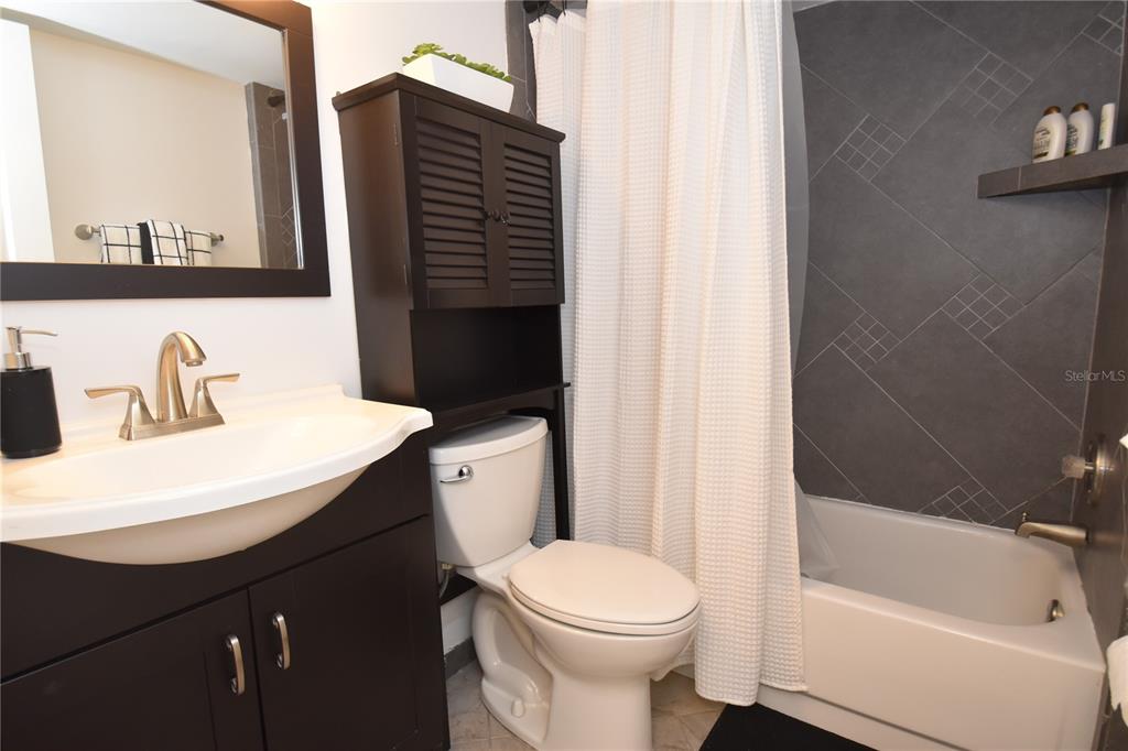 A bathroom features a dark vanity, a toilet with storage above, and a tiled shower — 1716 GLENHOUSE DRIVE UNIT GL323, SARASOTA, FL