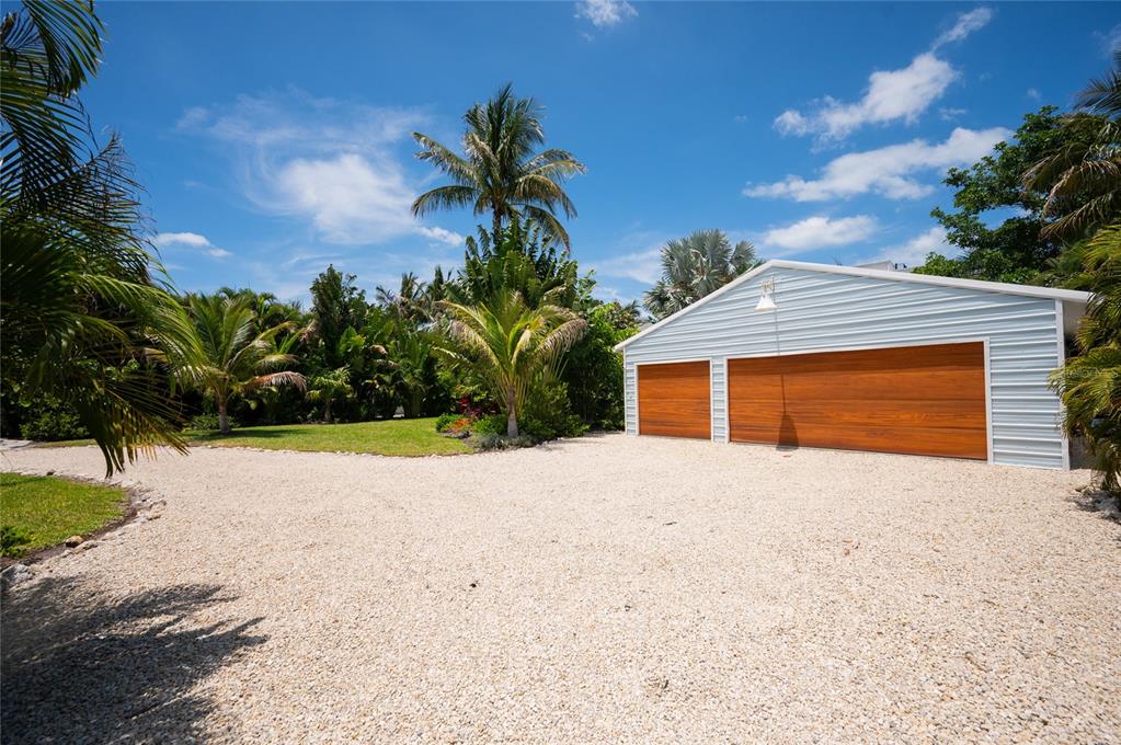 A gravel driveway leads to a detached garage with two wood-paneled doors and light siding — 240 GLADIOLUS STREET, ANNA MARIA, FL