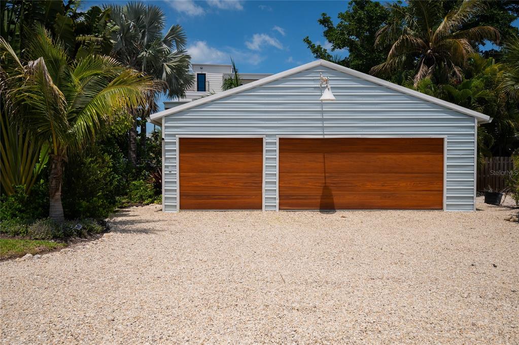 A detached two-car garage with light blue siding and wood-toned doors sits on gravel — 240 GLADIOLUS STREET, ANNA MARIA, FL