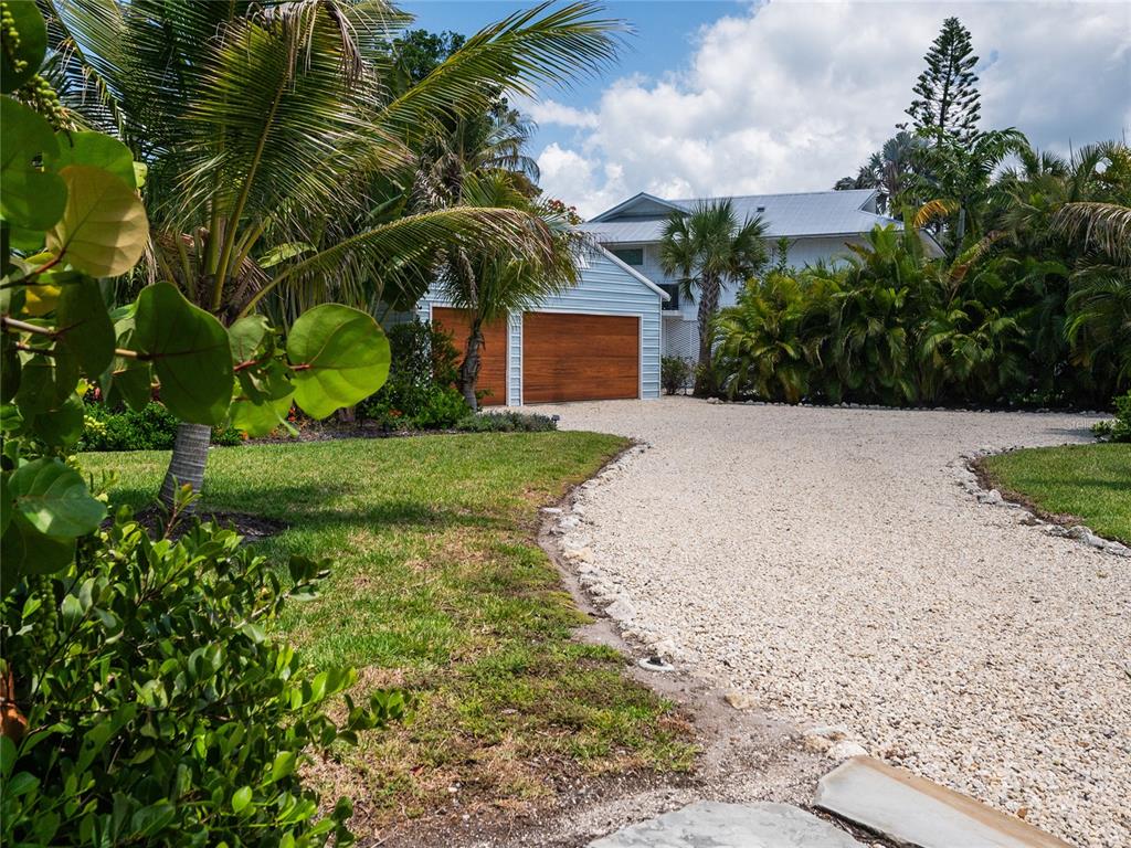 A gravel driveway leads to a two-car garage with wood doors at a white house — 240 GLADIOLUS STREET, ANNA MARIA, FL