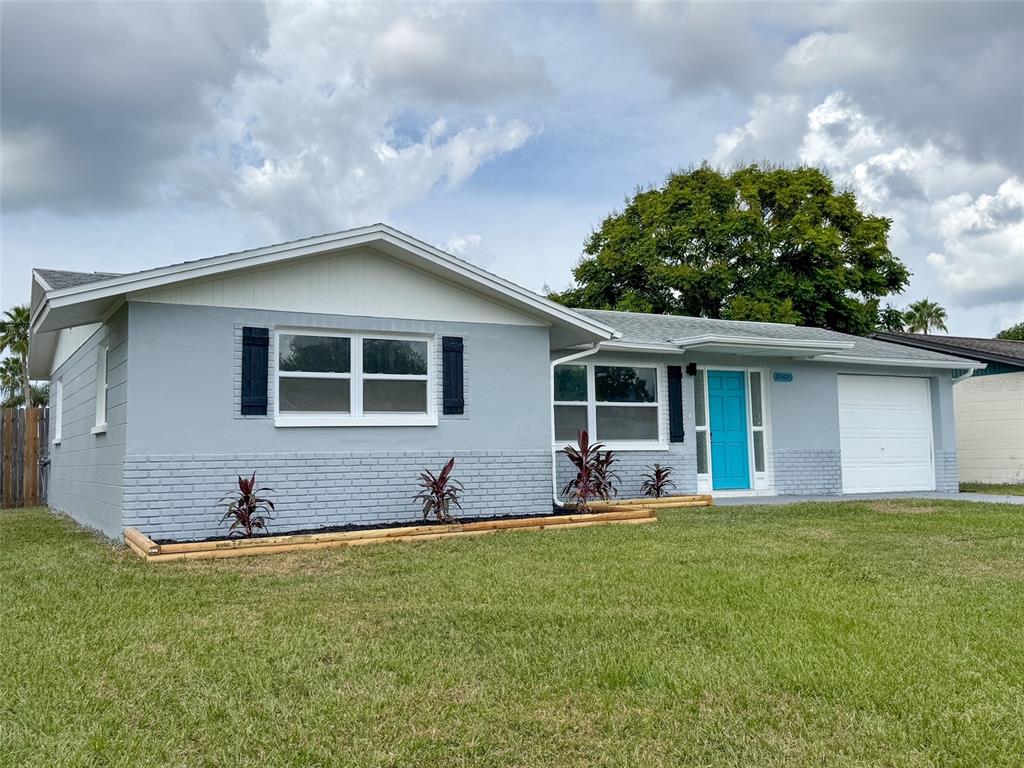 A single-story house with light blue siding, a bright blue front door, and a garage — 10805 FILLMORE AVENUE, PORT RICHEY, FL