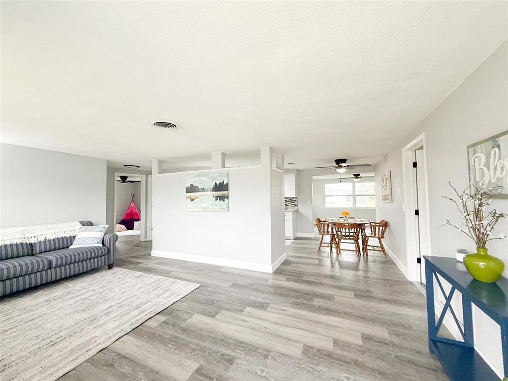 A living room with gray wood-look flooring flows into a dining area and kitchen — 10805 FILLMORE AVENUE, PORT RICHEY, FL