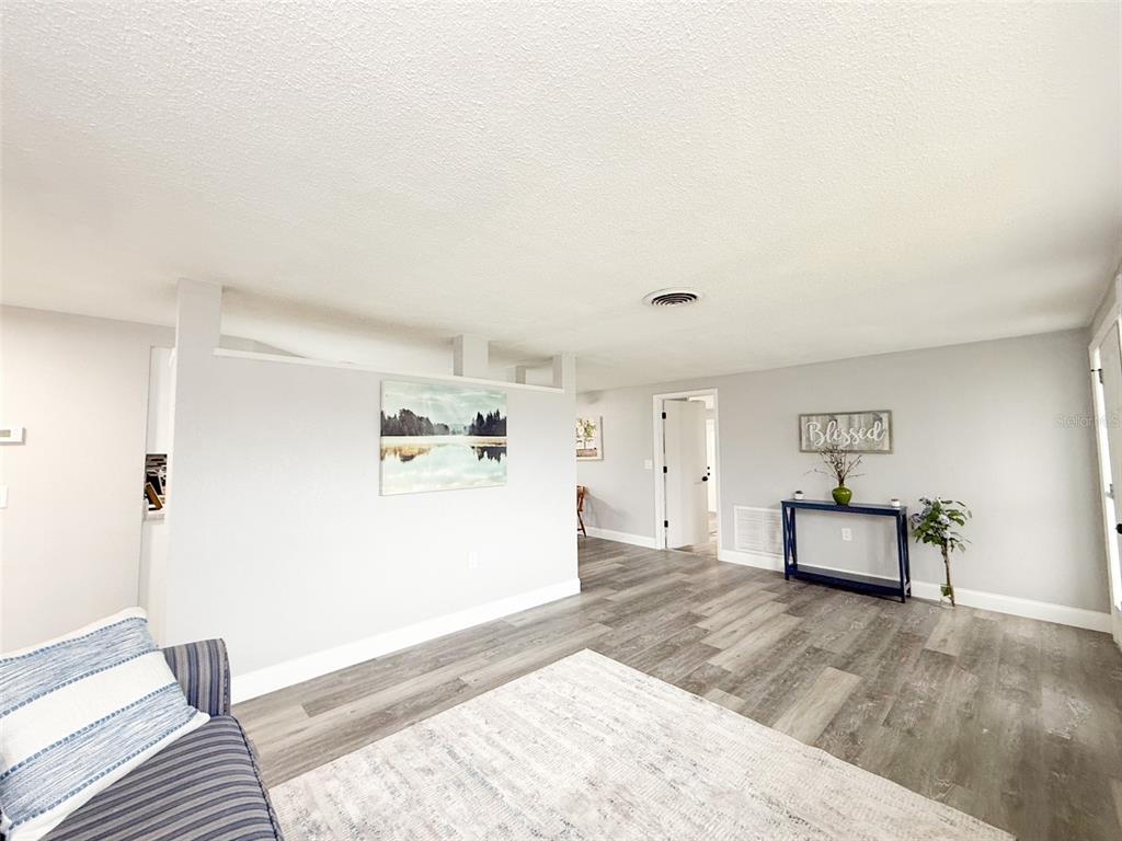 A living room features light gray walls, wood-look flooring, and a partial wall partition — 10805 FILLMORE AVENUE, PORT RICHEY, FL