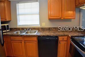 A kitchen features wood cabinets, a double sink, a black dishwasher, and a window — 1000 S SEMORAN BOULEVARD UNIT 408, WINTER PARK, FL