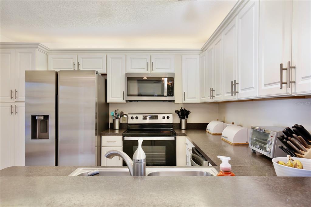A kitchen features white cabinets, stainless steel appliances, and dark countertops with a sink island — 600 NORTHERN WAY UNIT 1608, WINTER SPRINGS, FL