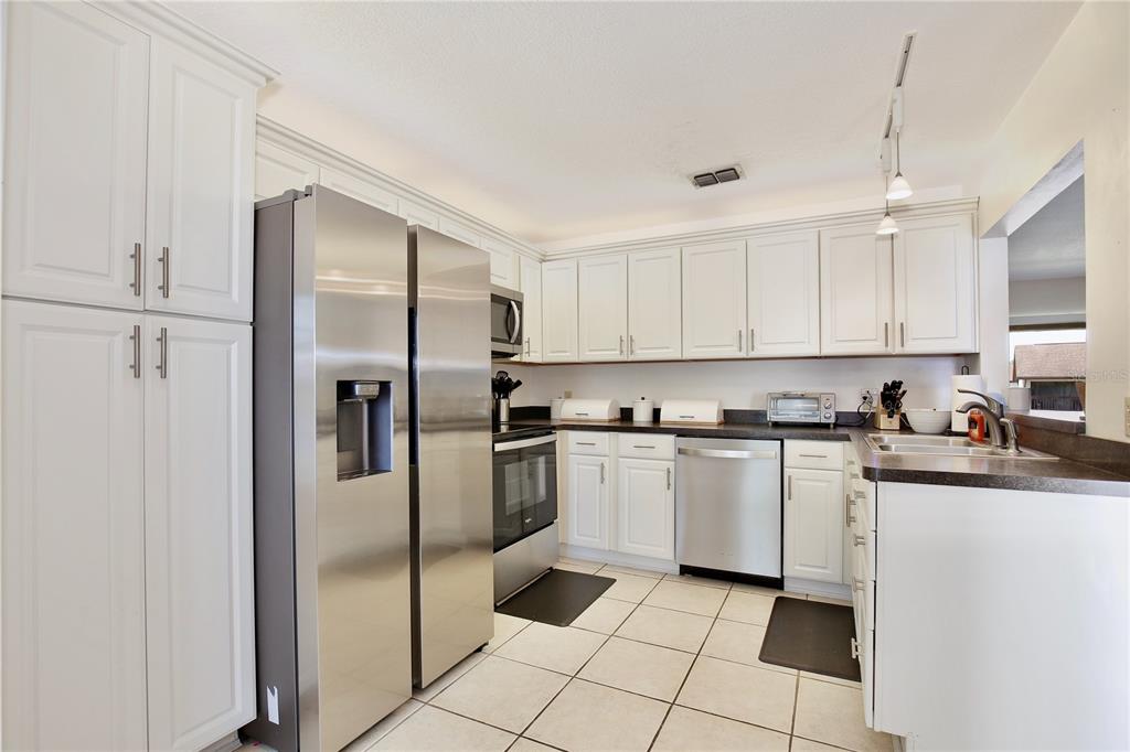 A kitchen features white cabinets, stainless steel appliances, dark countertops, and light-colored floor tiles — 600 NORTHERN WAY UNIT 1608, WINTER SPRINGS, FL
