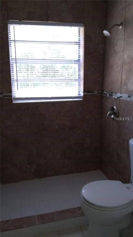 A bathroom features a tiled walk-in shower with a window and a white toilet — 5036 COLLEGE, ORLANDO, FL