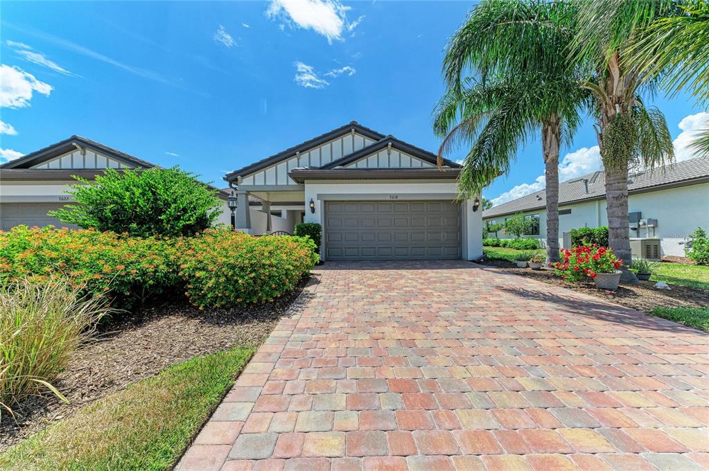 A single-story house with a paved driveway, a two-car garage, and landscaping under a blue sky — 7018 HOLBROOK COVE, BRADENTON, FL