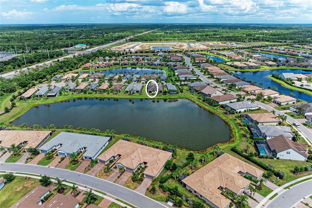 An aerial view shows a residential neighborhood with houses surrounding a central lake — 7018 HOLBROOK COVE, BRADENTON, FL