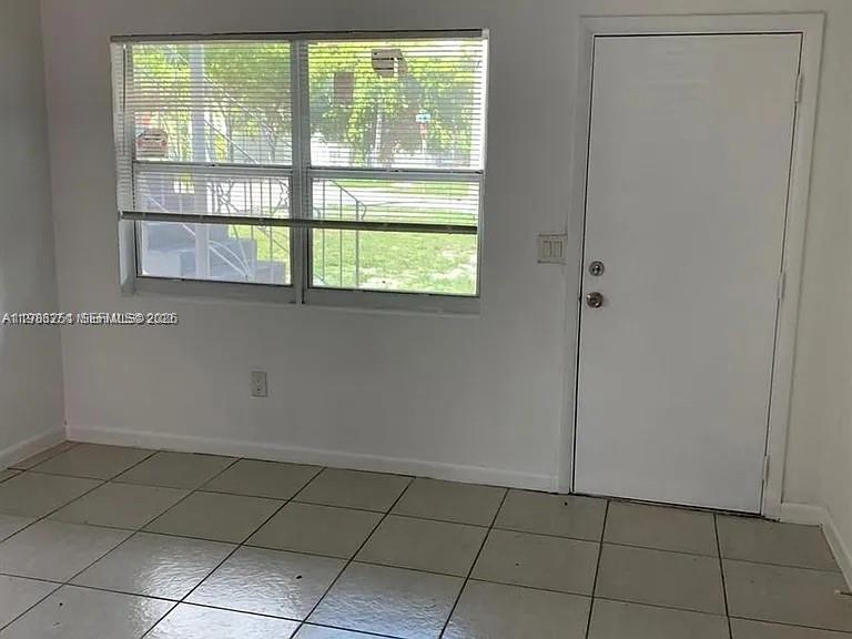 A room with white walls, tiled flooring, a window with blinds, and a white door — 1277 NW 58th St, Miami FL 33142, MIAMI, FL