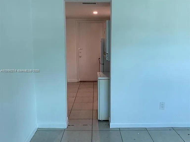 A view through a doorway shows a tiled utility area with a stacked washer and dryer — 1277 NW 58th St, Miami FL 33142, MIAMI, FL