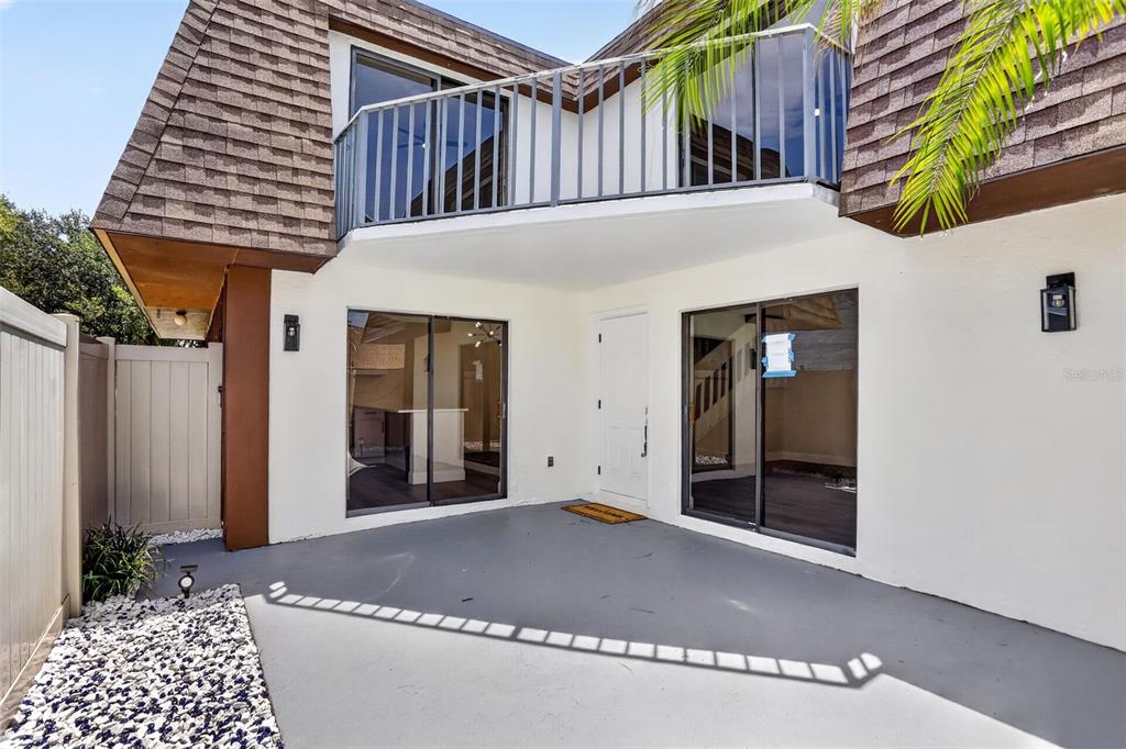 A ground-level patio with a white door, two sliding glass doors, and an upper balcony — 4075 SHANNON BROWN DRIVE, ORLANDO, FL