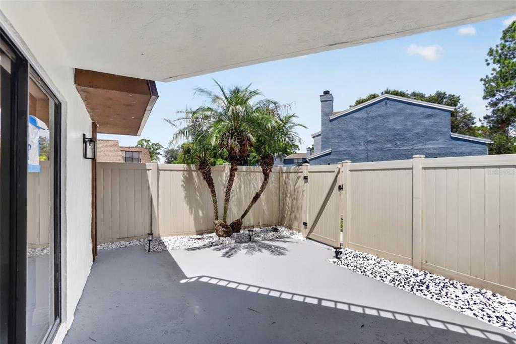 A concrete patio features a small palm tree, white gravel, and a tan privacy fence — 4075 SHANNON BROWN DRIVE, ORLANDO, FL