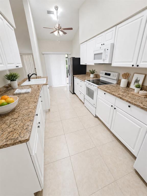 A galley kitchen features white cabinets, granite countertops, and stainless steel appliances — 1203 SAXONY CIRCLE UNIT B, PUNTA GORDA, FL