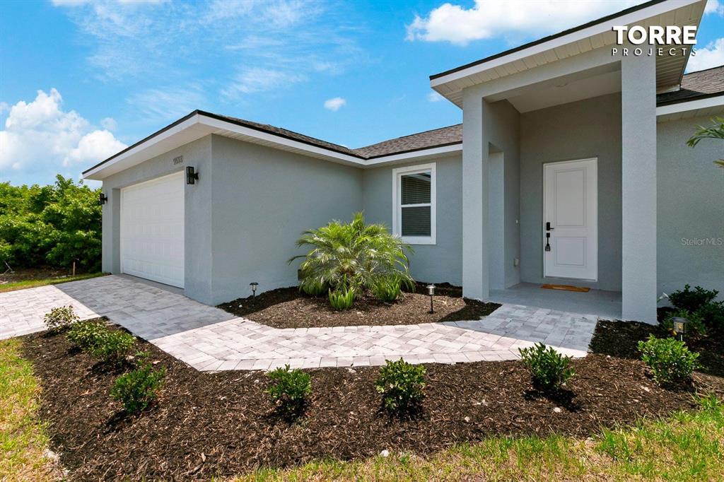 The exterior of a gray house features a white garage door, a front entrance, and landscaping — 14024 WENZEL AVENUE, PORT CHARLOTTE, FL