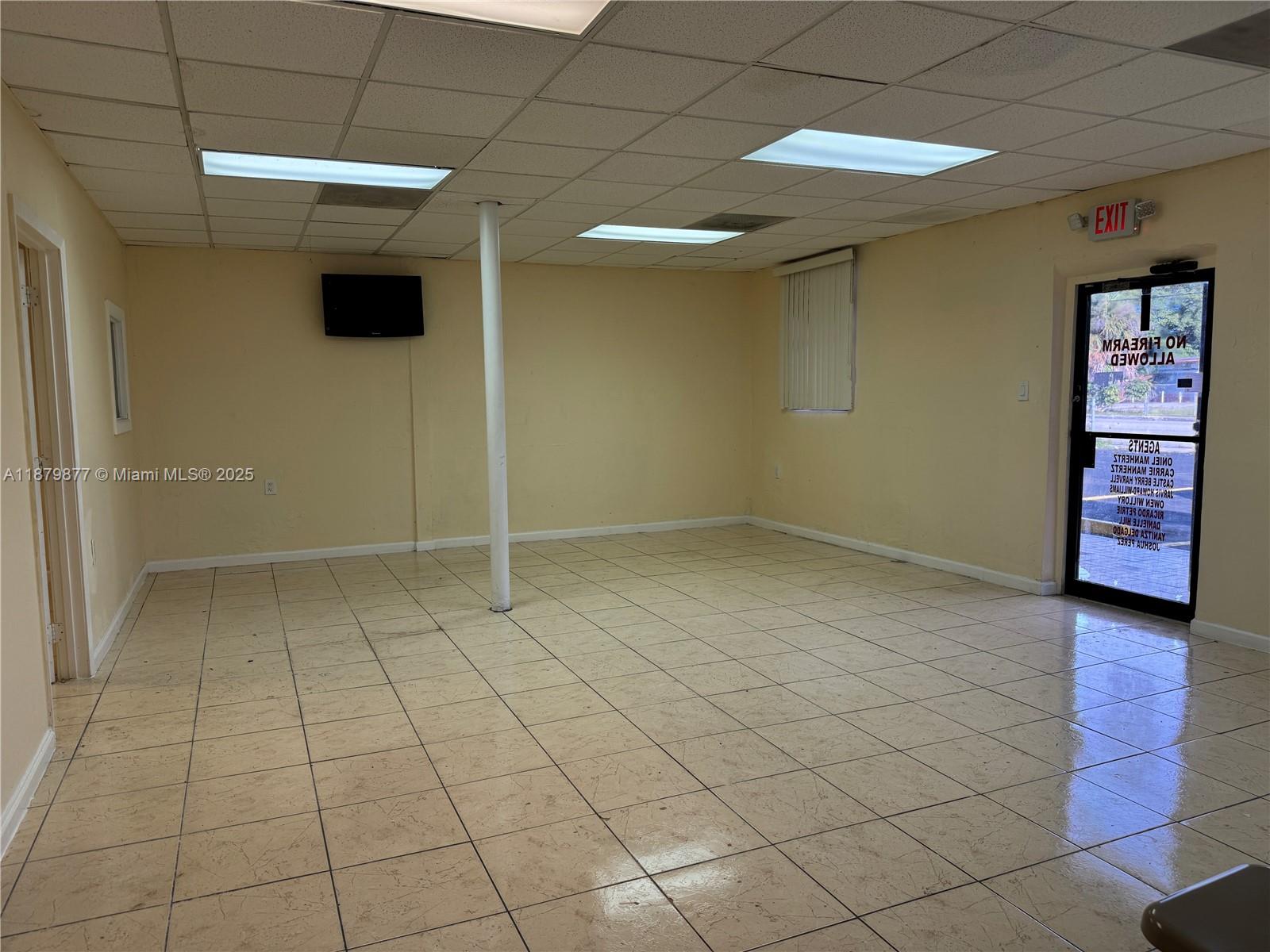 An empty commercial space features beige tile flooring, a central support column, and an exit door — 1605 NW 95th St, Miami FL 33147, MIAMI, FL