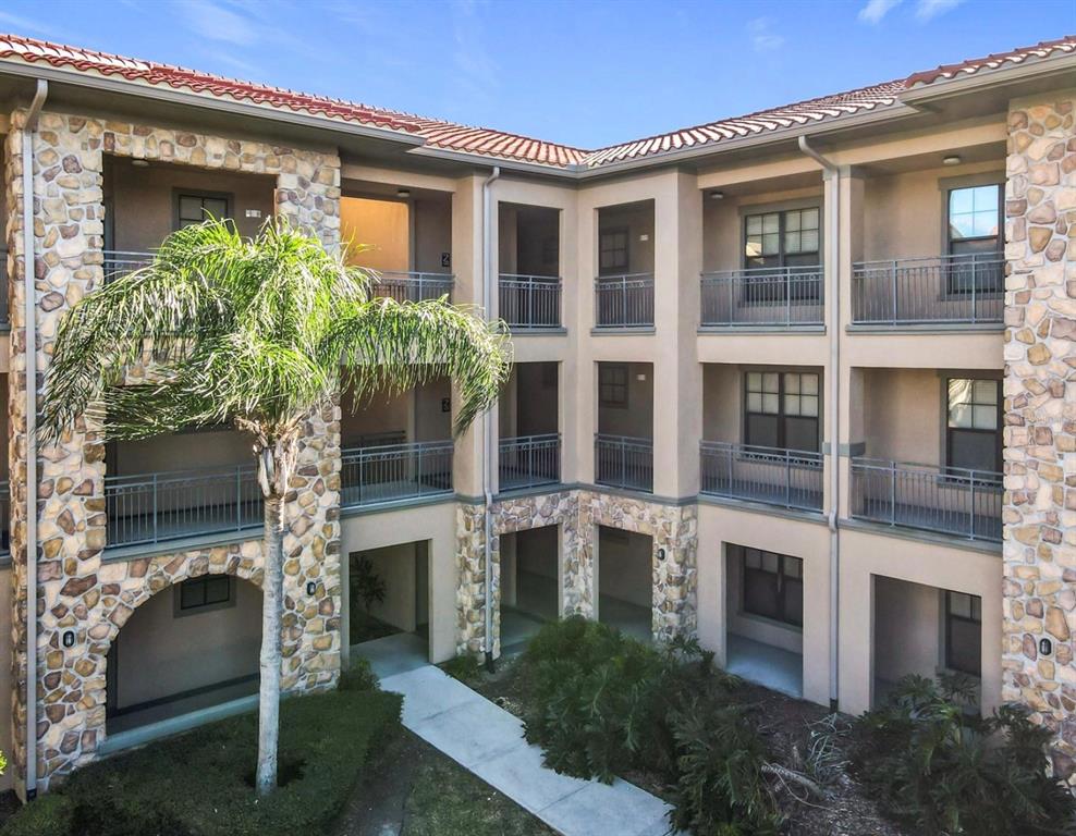 A multi-story apartment building exterior features stone accents, balconies with metal railings, and a palm tree — 903 CHARO PARKWAY UNIT 837, DAVENPORT, FL
