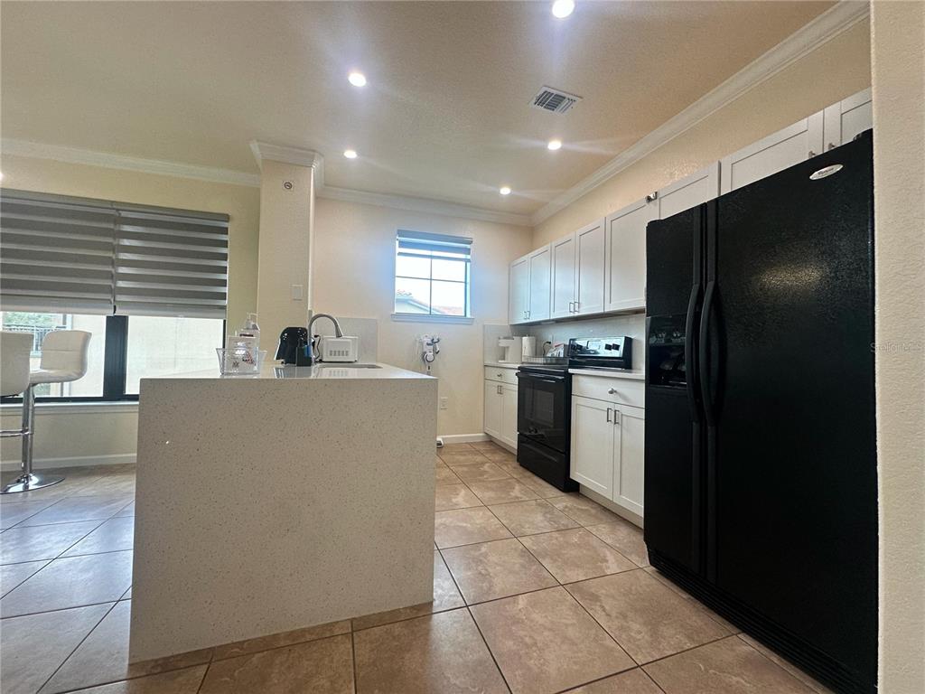 A kitchen features white cabinetry, a large island, black appliances, and light-colored tile flooring — 903 CHARO PARKWAY UNIT 837, DAVENPORT, FL
