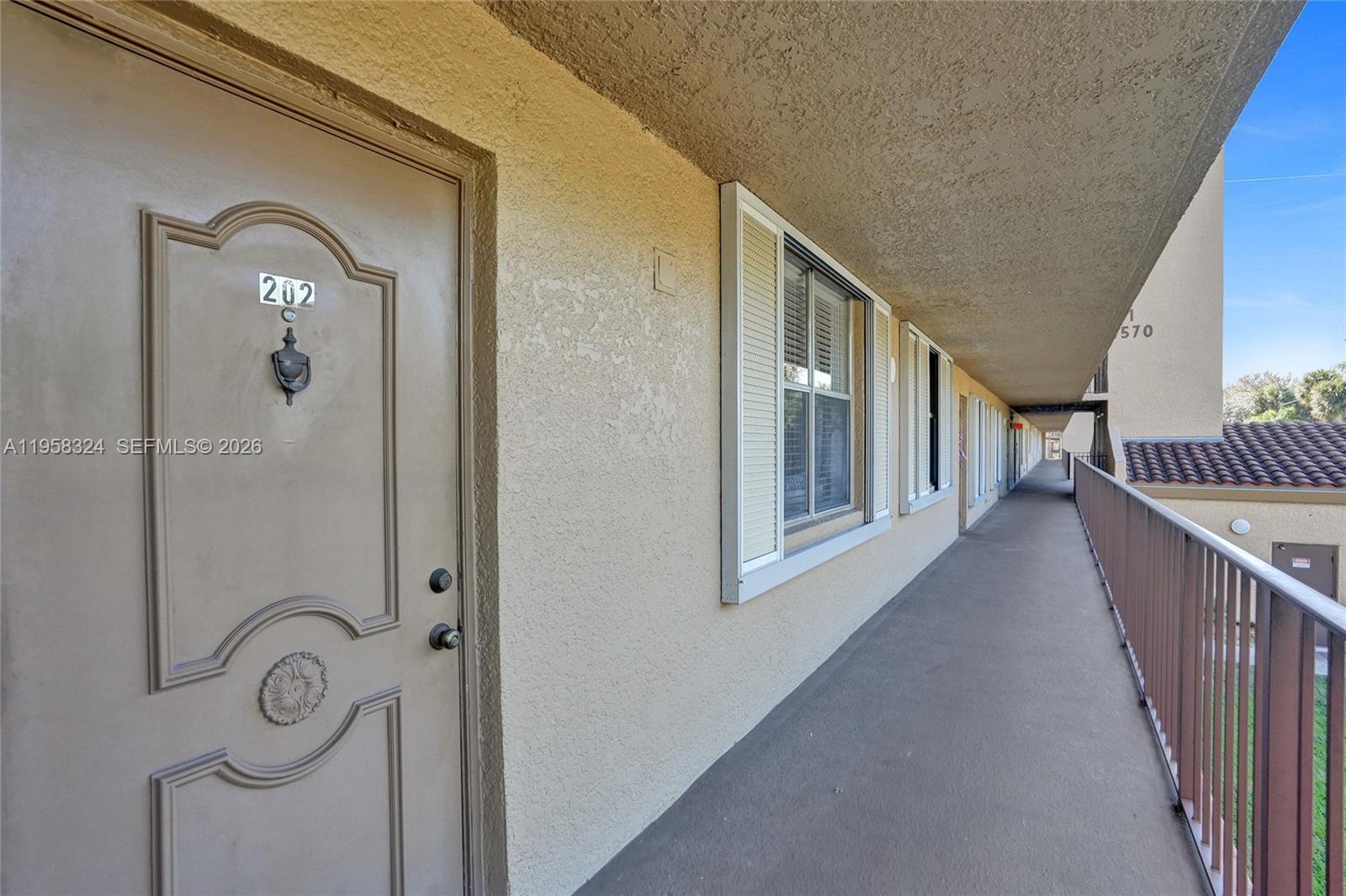 An exterior walkway leads past a brown door labeled 202 toward a building corridor — 4570 NW 18th Avenue # 202, Deerfield Beach FL 33064, DEERFIELD BEACH, FL