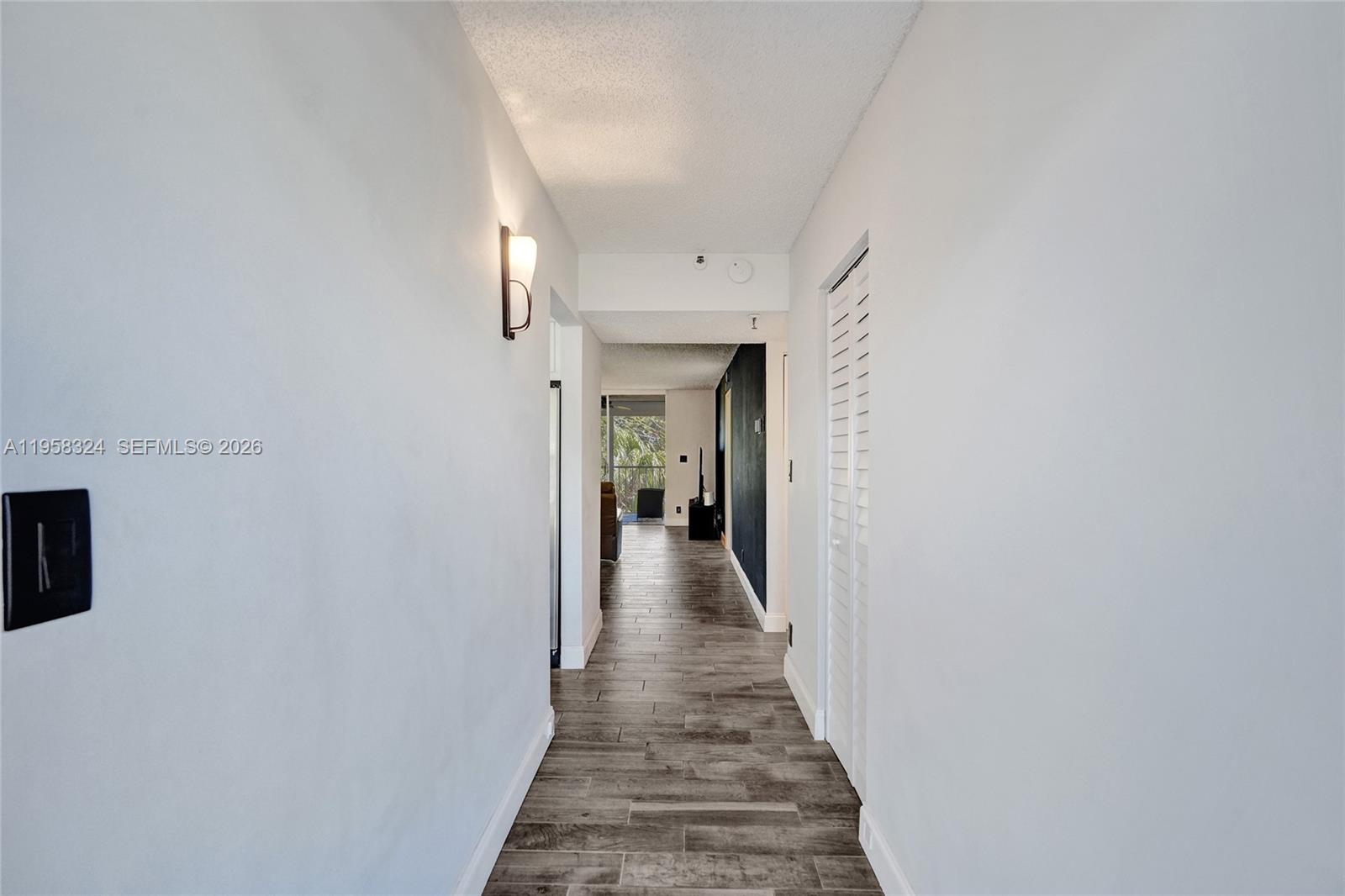 A hallway with wood-look tile flooring leads toward a living area with a balcony — 4570 NW 18th Avenue # 202, Deerfield Beach FL 33064, DEERFIELD BEACH, FL