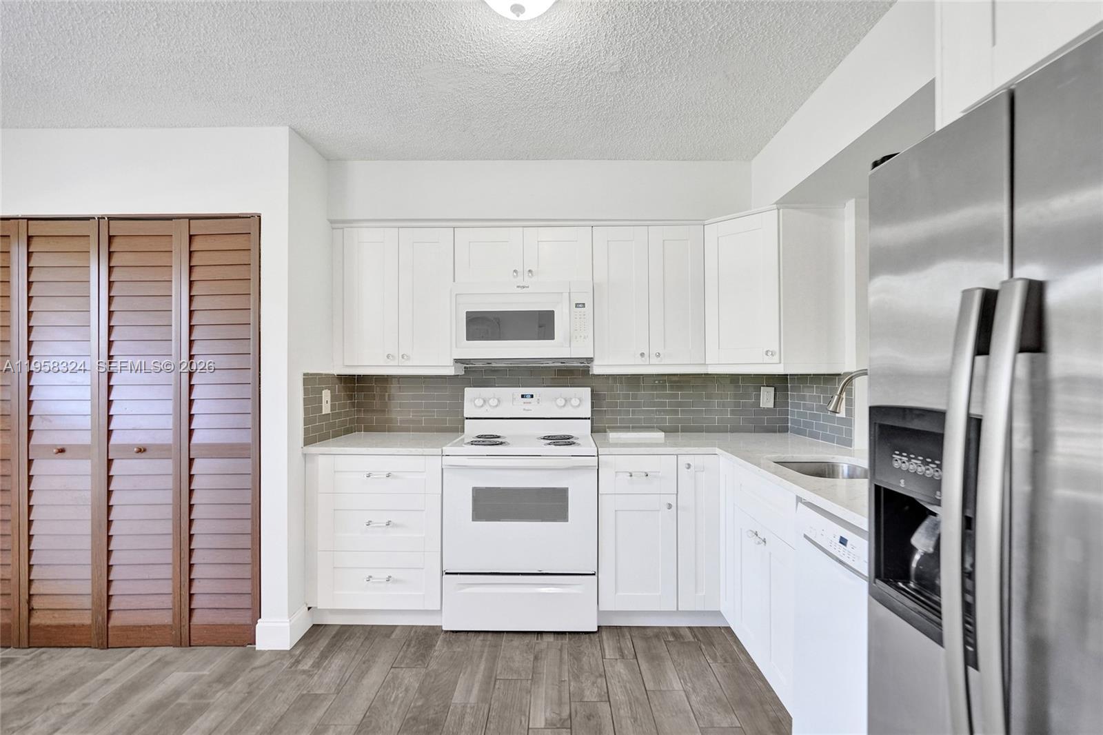 A kitchen features white cabinets, a white stove, a gray tiled backsplash, and wood-look flooring — 4570 NW 18th Avenue # 202, Deerfield Beach FL 33064, DEERFIELD BEACH, FL