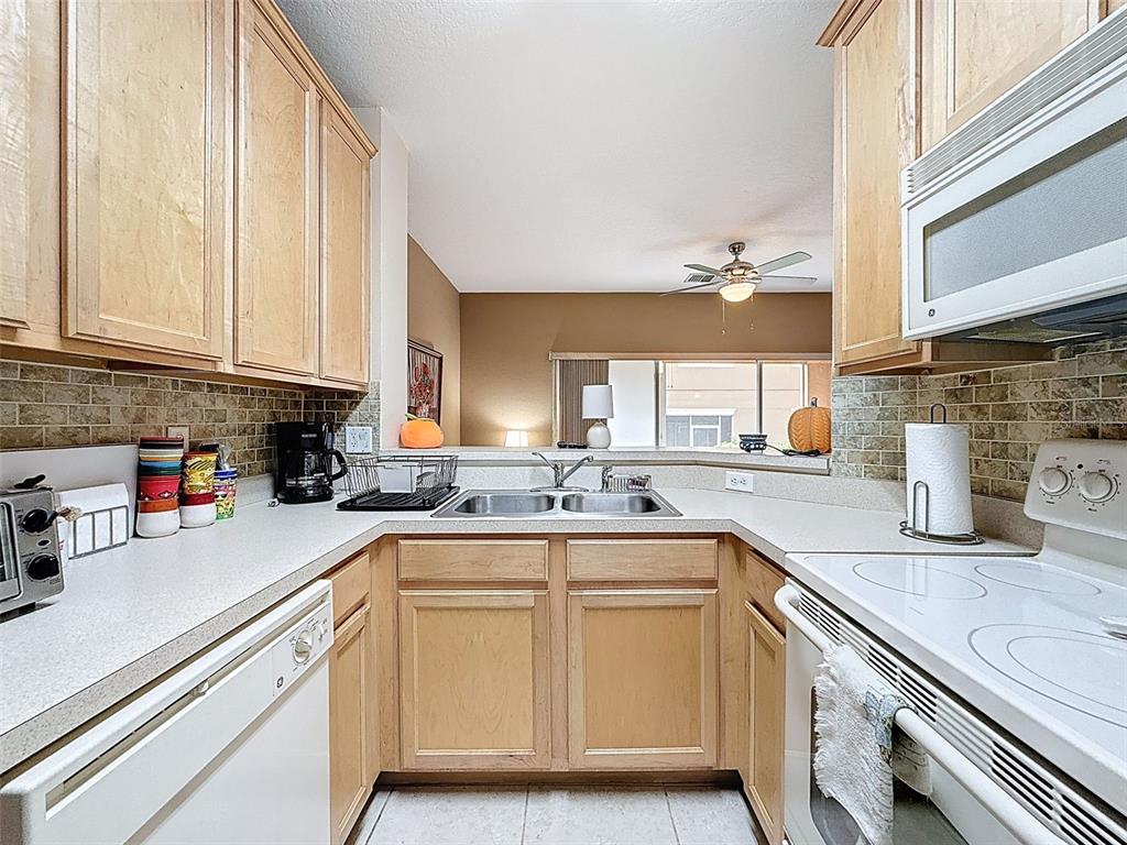 A kitchen features light wood cabinets, white appliances, a double sink, and tiled backsplash — 335 BEXLEY DRIVE, DAVENPORT, FL