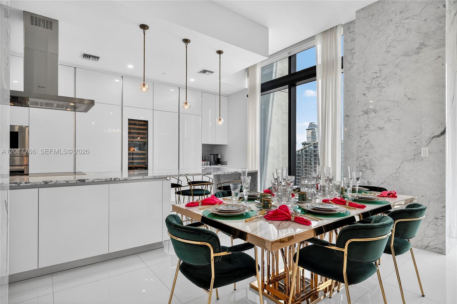 A modern kitchen and dining area features white cabinetry, marble surfaces, and green velvet chairs — 88 SW 7th St, Miami FL 33130, MIAMI, FL